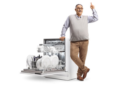 Smiling mature man with a dishwasher and a pile of plates pointing up isolated on white backgroundの写真素材