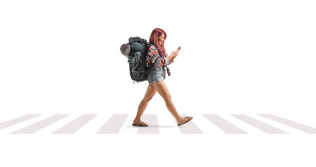 Female backpacker using a smartphone and walking at zebra crossing isolated on white backgroundの写真素材