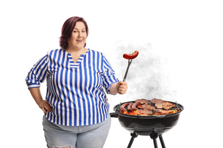 Chubby woman grilling sausage on a bbq isolated on white backgroundの写真素材