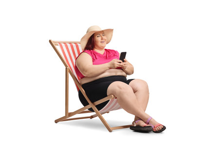 Corpulent woman sitting in a lounge chair and holding a smartphone isolated on white backgroundの写真素材