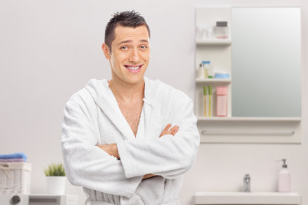 Young man in a bathroom posing in a white bathrobe
