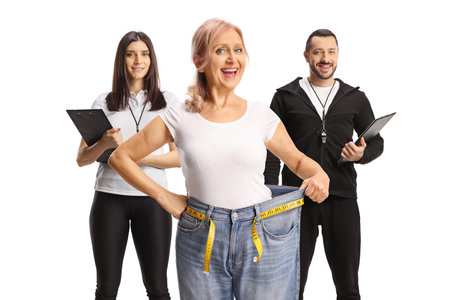 Happy woman after weight loss posing with personal trainers isolated on white background