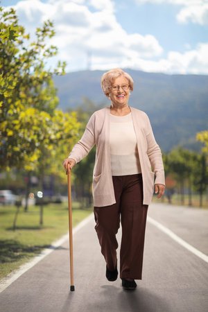 Smiling elderly woman walking in a park with a caneの写真素材