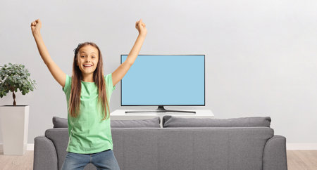 Excited kid at home gesturing happiness in front of a tv screenの写真素材