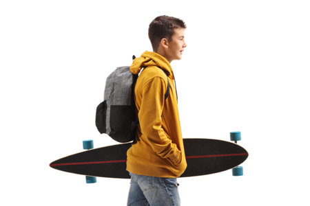 Teenage student in a yellow hoodie walking and holding a longboard isolated on white backgroundの写真素材