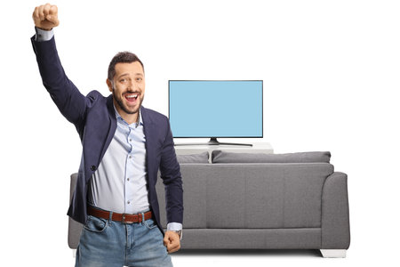 Excited young man gesturing happiness in front of a tv isolated on white backgroundの写真素材