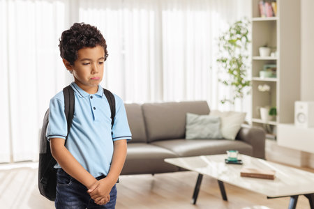 Sad boy with a backpack standing alone at home in a living roomの写真素材
