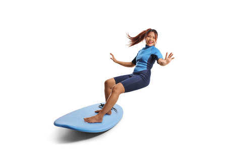 Woman in a wetsuit riding a surfboard isolated on white backgroundの写真素材