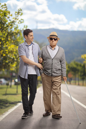 Young man helping an elderly blind man in a parkの写真素材