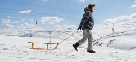Full length profile shot of a man in winter clothes pulling a sled on a mountain