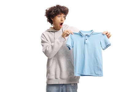 Shocked young man holding a small blue t-shirt isolated on white backの写真素材