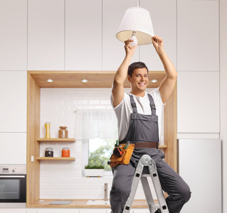Repairman seated on a ladder changing a light bulb on a kitchen ceiling and smilingの写真素材