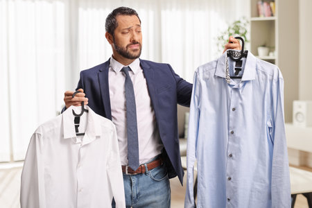 Doubtful man in a living room choosing which shirt to wearの写真素材