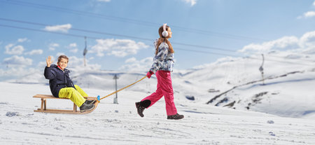 Girl pulling a boy with a sled on a snowy mountainの写真素材