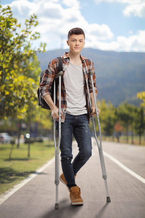 Full length portrait of a male student with crutches standing in a parkの写真素材