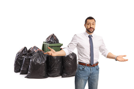 Disappointed man standing in front of a pile of waste bags isolated on white backgroundの写真素材