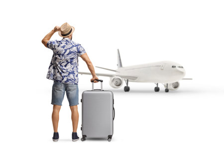 Rear view shot of a tourist waiting with a suitcase and looking at a plane isolated on white backgroundの写真素材