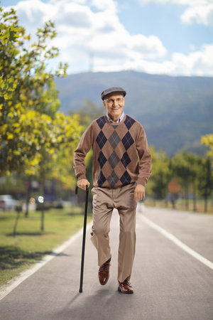 Full length portrait of an elderly man with a cane walking in a parkの写真素材