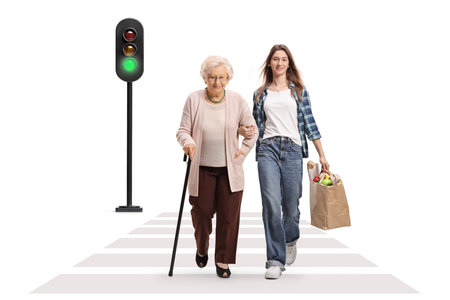 Young female carrying a grocery bag and walking with a senior woman at zebra crossing isolated on white backgroundの写真素材