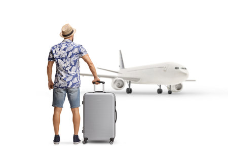 Rear view shot of a man waiting with a suitcase and looking at a plane isolated on white backgroundの写真素材
