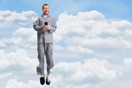 Man in pajamas jumping in the sky and clouds and holding a smartphone