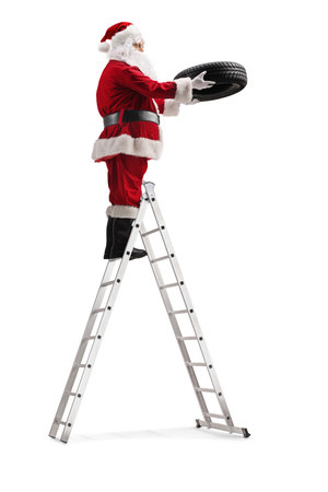 Santa claus standing on a ladder and holding a car tire isolated on white backgroundの写真素材