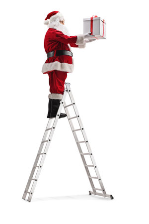 Santa claus standing on top of a ladder and holding a gift box isolated on white backgroundの写真素材