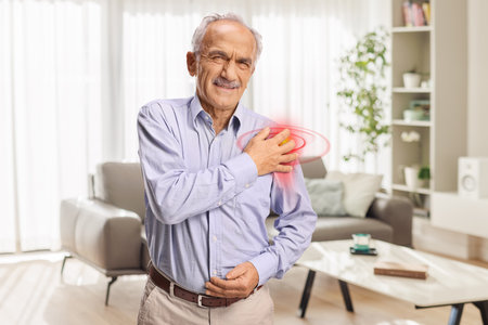 Elderly man with pain in shoulder standing at homeの写真素材