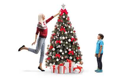 Son watching his mother decorating a Christmas tree isolated on white backgroundの写真素材