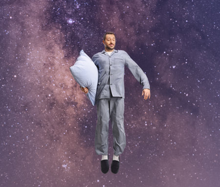 Man in pajamas holding a pillow and jumping to the starsの写真素材