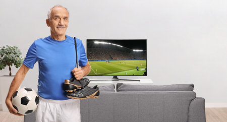 Elderly man with football equipment in a room with tv and sofaの写真素材