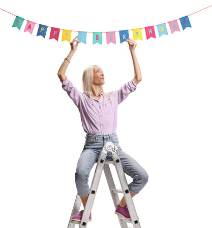 Woman on a ladder hanging birthday decoration flags isolated on white backgroundの写真素材
