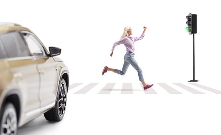 Full length profile shot of a woman running over zebra crossing at green traffic light isolated on white backgroundの写真素材