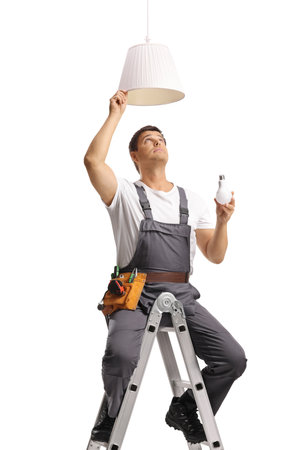 Repairman seated on a top of a ladder fixing a bulb on a pendant lamp isolated on white backgroundの写真素材