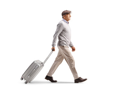 Full length profile shot of an elderly gentleman walking and pulling a suitcase isolated on white backgroundの写真素材