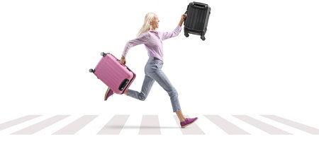 Woman at zebra crossing running with two suitcases isolated on white backgroundの写真素材