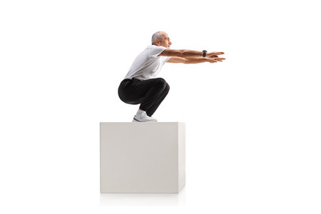 Mature man exercising on a white cube isolated on white backgroundの写真素材