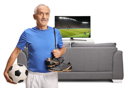 Elderly man with football equipment in front of a tv and sofa isolated on white backgroundの写真素材