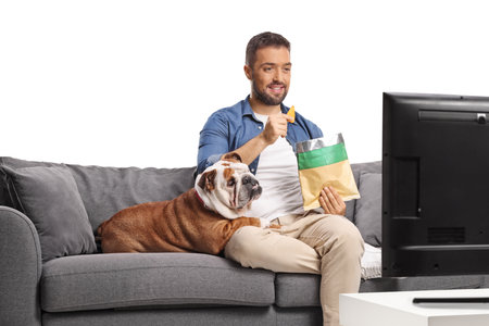 Man eating crisps on a sofa with a bulldog and watching tv isolated on white backgroundの写真素材