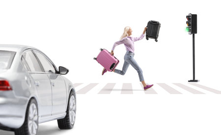 Woman at zebra crossing running with two suitcases in front of a car isolated on white backgroundの写真素材