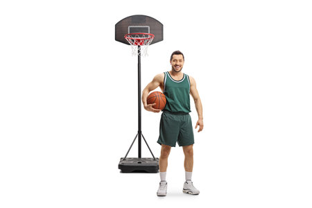 Full length portrait of a basketball player holding a ball in front of a basket net isolated on white backgroundの写真素材