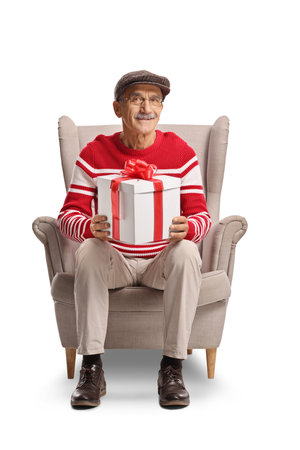 Elderly man sitting in an armchair and holding a present isolated on white backgroundの写真素材