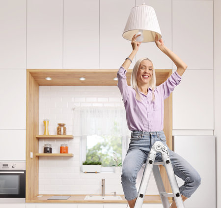 Woman sitting on a ladder putting a light bulb in a pendant lampの写真素材