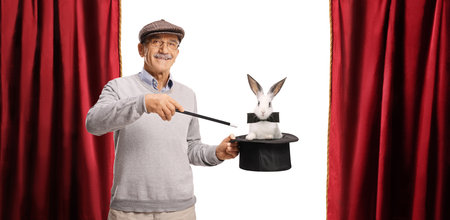 Elderly man performing a magic trick with hat and a rabbit on stage isolated on white backgroundの写真素材