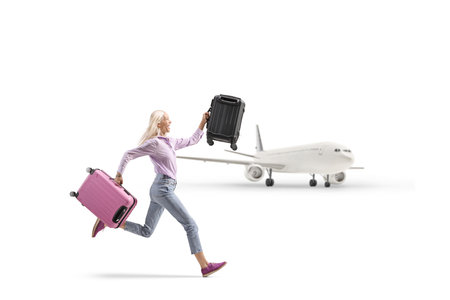 Woman running with two suitcases in front of a plane isolated on white backgroundの写真素材