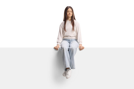 Teenage girl sitting on a blank panel isolated on white backgroundの写真素材