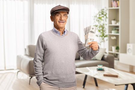 Pensioner holding stacks of money banknotes at homeの写真素材