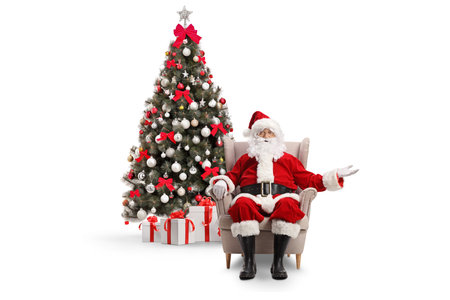Santa claus sitting in armchair in front of a decorated christmas tree isolated on white backgroundの写真素材