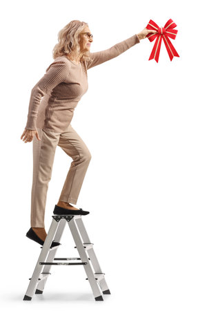 Woman on a ladder hanging a red bow isolated on white backgroundの写真素材