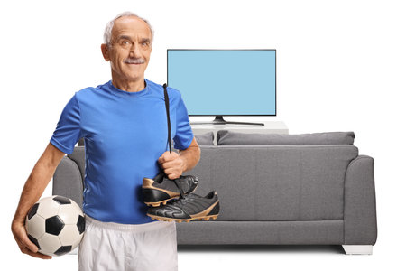 Elderly man with football equipment for training in front of a tv and sofa isolated on white backgroundの写真素材